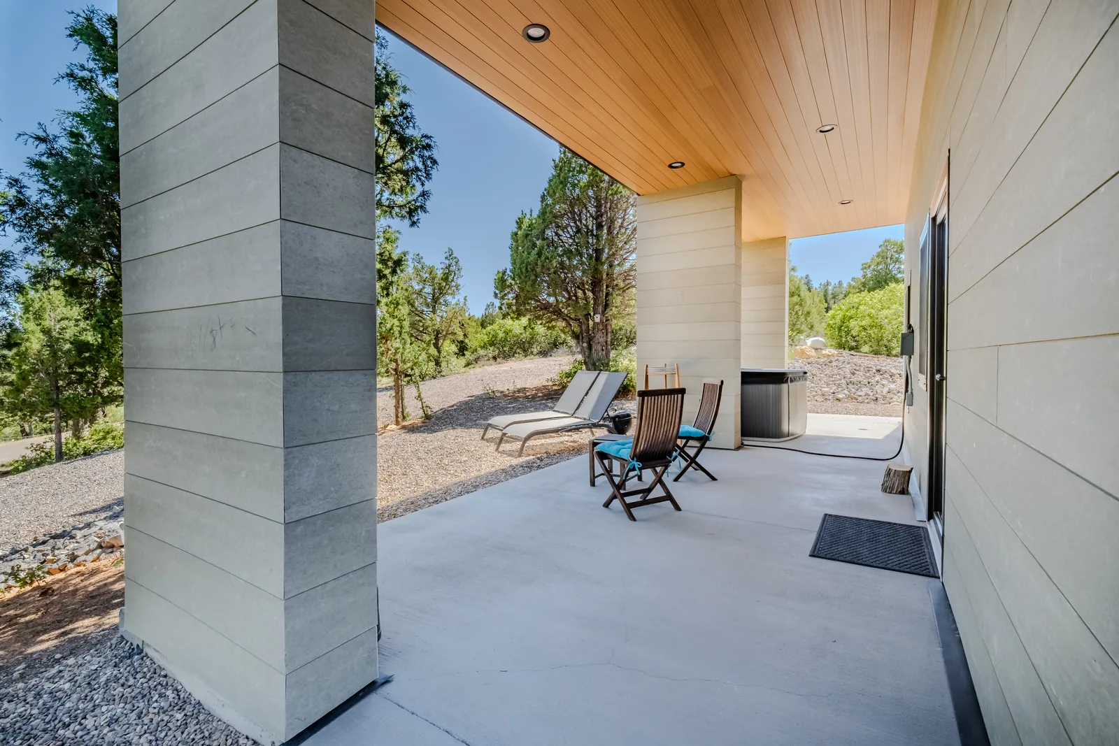 Covered concrete-and-wood entry patio of a modern custom home on a wooded hillside